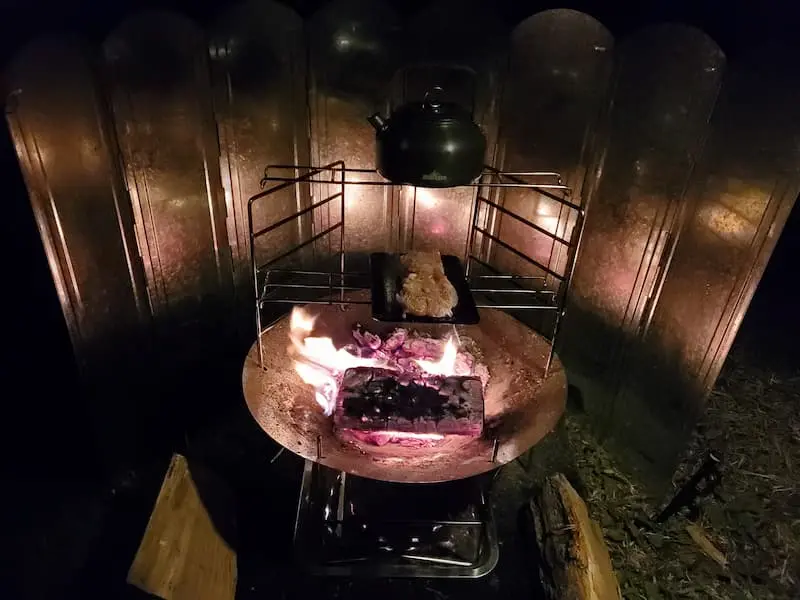 上段でお湯を沸かし下段で肉を焼いているsolotour焚き火台のが画像です。